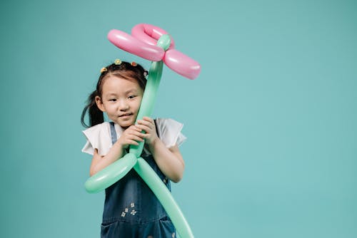 Girl in Blue Denim Sundress Holding Pink and Green Balloon Figure