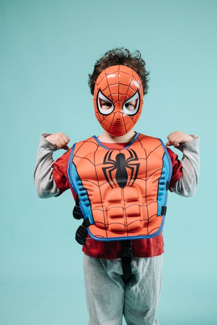 Child wearing a superhero costume, posing confidently in a studio setting.