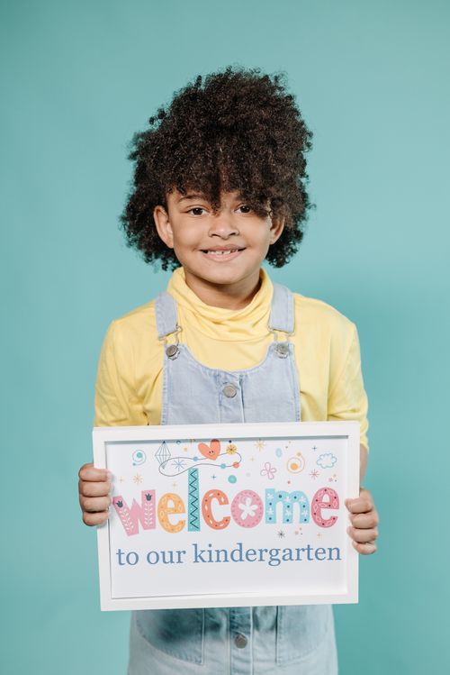 Free Adorable child holding a 'Welcome to our kindergarten' sign against a teal background. Stock Photo