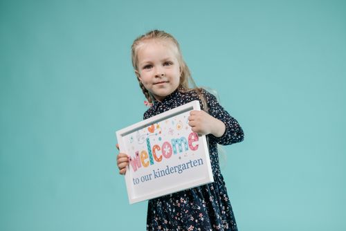 Free A cheerful girl poses with a welcome sign against a light teal background. Stock Photo