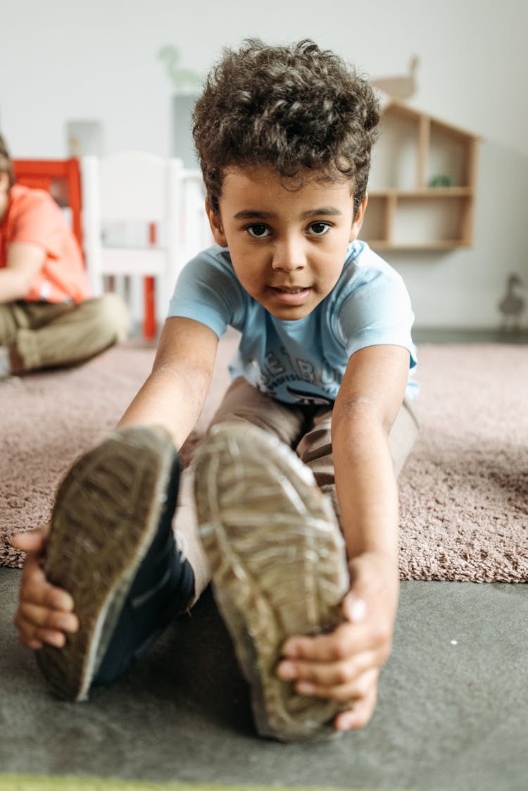 Boy In Blue Shirt Sitting On The Carpet While Holding His Toes