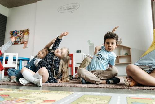 Free Children in a diverse classroom raising hands during a group activity indoors. Stock Photo