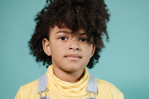 Free Adorable young child with afro hair posing in front of a turquoise background. Stock Photo
