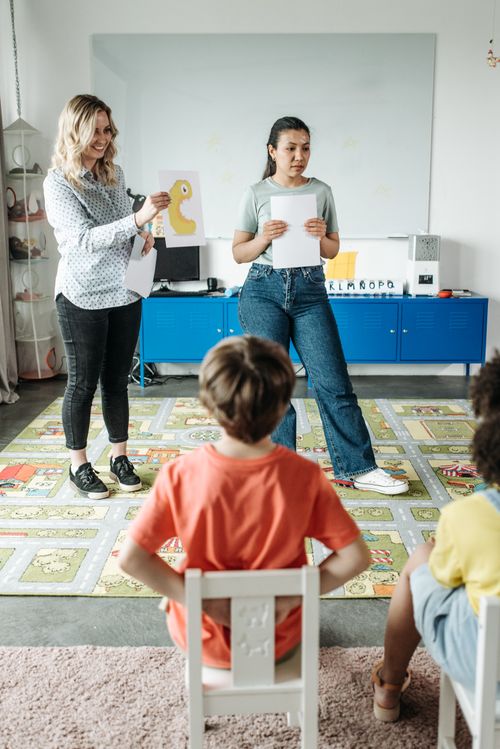 Free Two teachers interacting with children in a brightly lit classroom setting. Stock Photo
