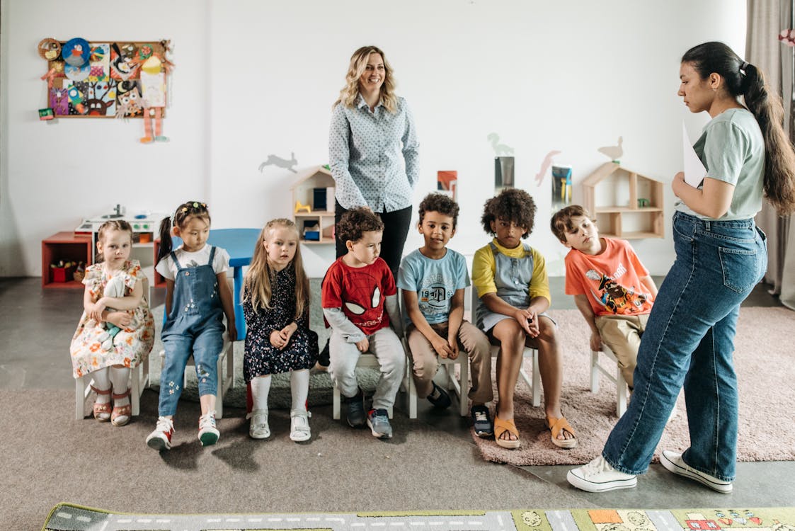 Free Group of Children Sitting on White Chairs Stock Photo