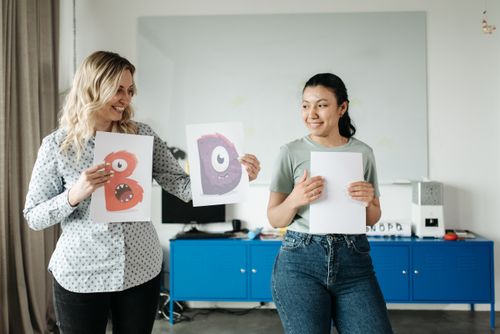 Free Two teachers holding fun monster drawings in a classroom setting. Stock Photo