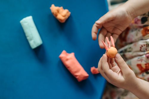 Free Young hands shaping colorful clay into fun figures on a vibrant blue background. Stock Photo