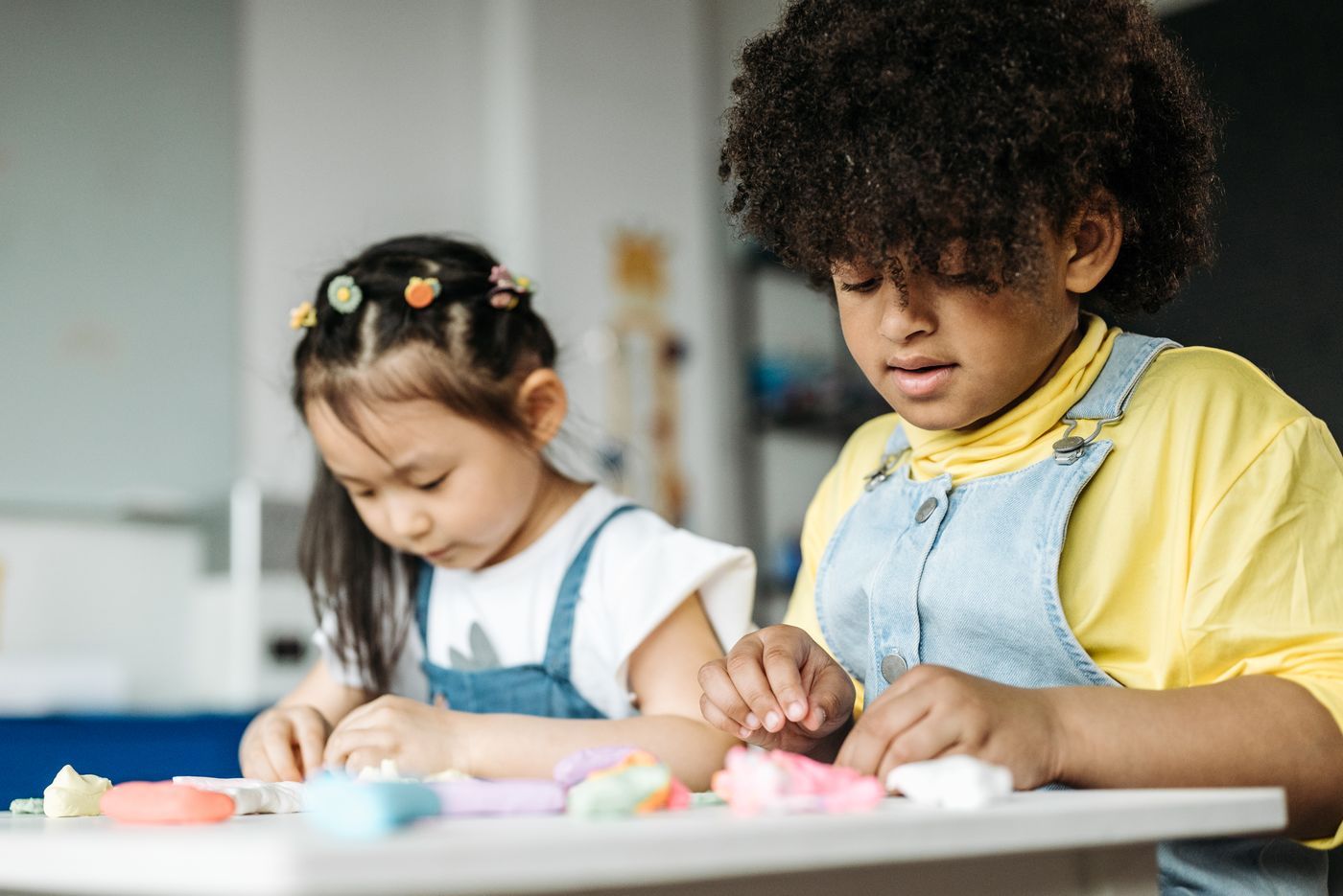 Dos niños jugando y creando figuras con plastilina de colores alrededor de una mesa en el aula