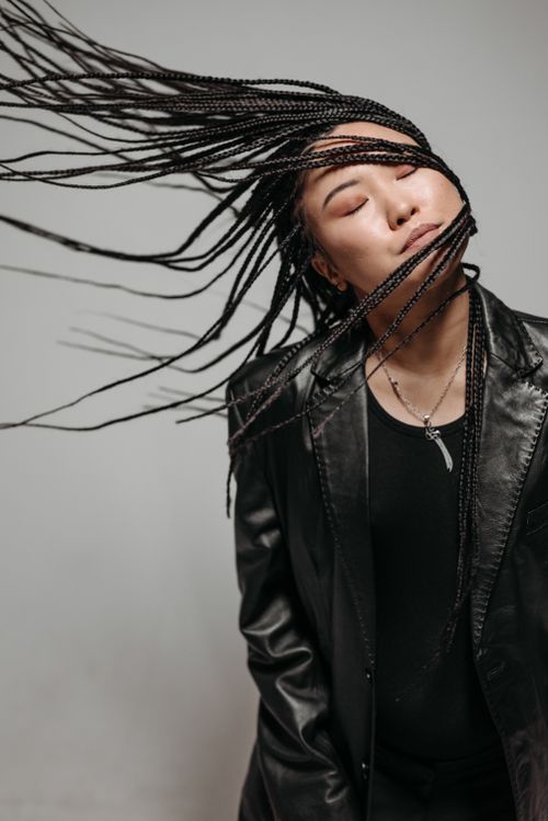 Free A vibrant portrait of an Asian woman in a leather jacket flipping her braided hair. Stock Photo