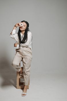 Elegant woman in modern outfit posing in studio holding a donut playfully.