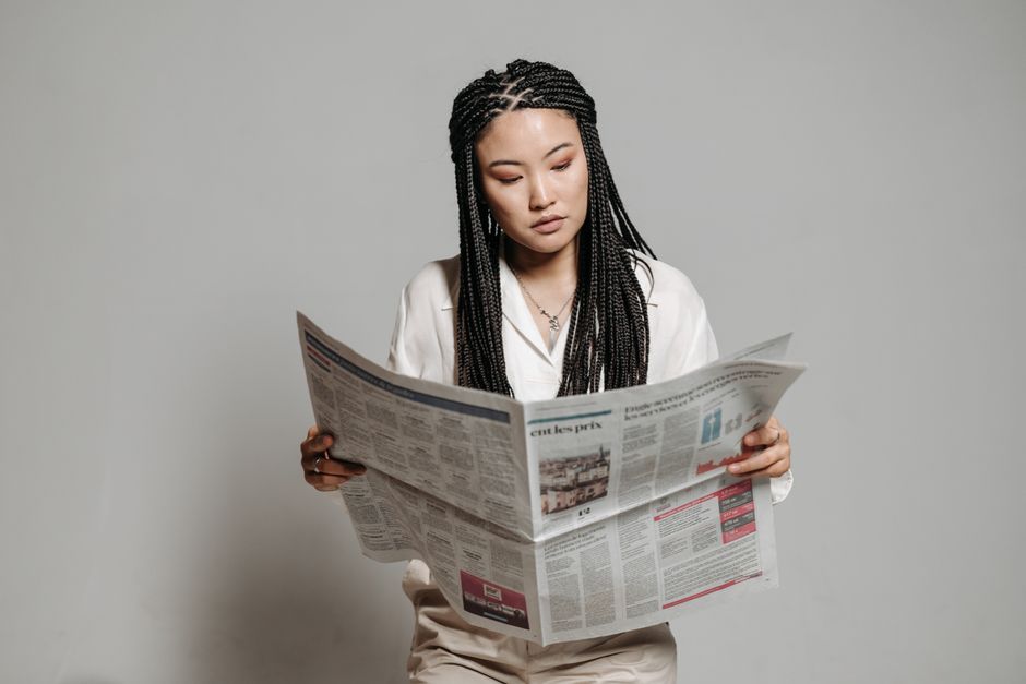Woman with braided hairstyle reading a newspaper indoors, showing leisure and focus.
