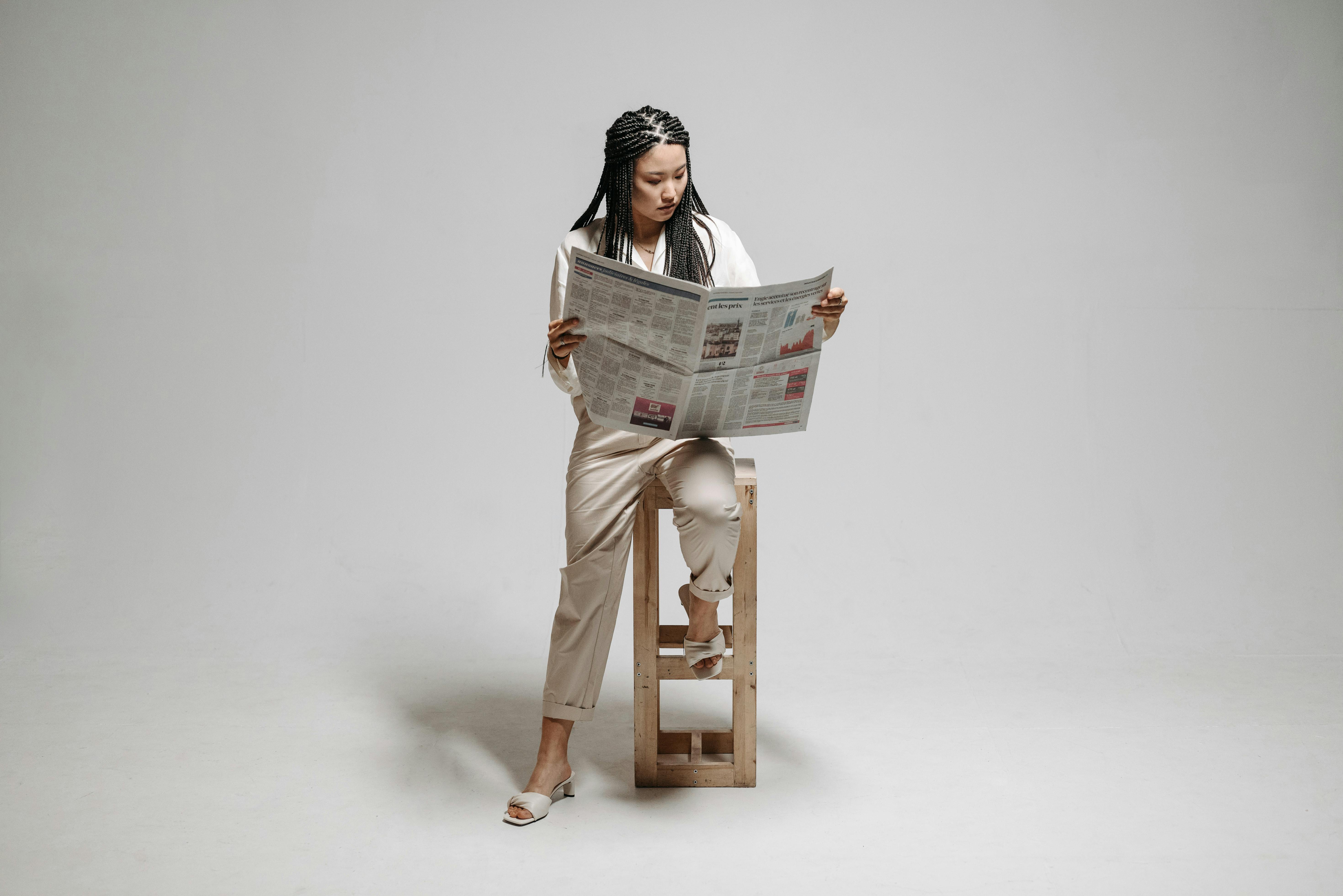 a woman sitting on a wooden chair while reading newspaper