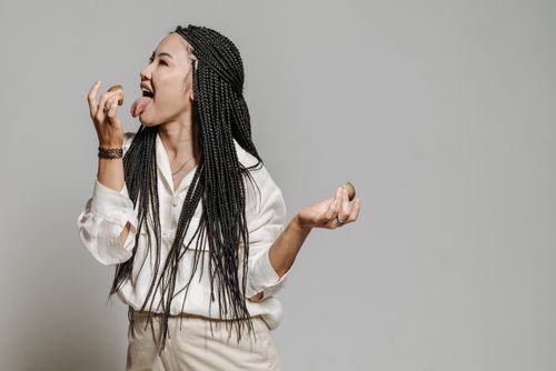 Free Fashionable woman with long braided hair posing and licking a small object in studio. Stock Photo