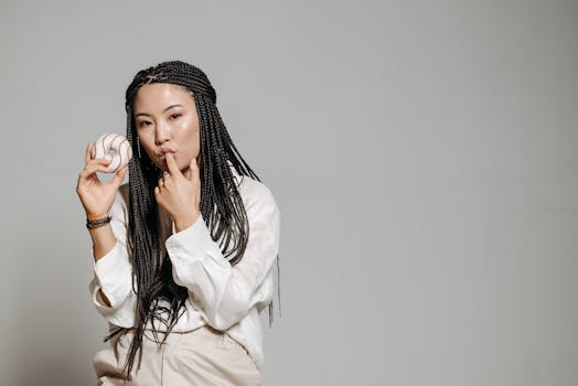 Asian woman with long braids holding a donut and posing against a plain grey background.