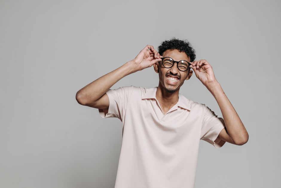 A cheerful man wearing glasses and a light shirt, smiling indoors.