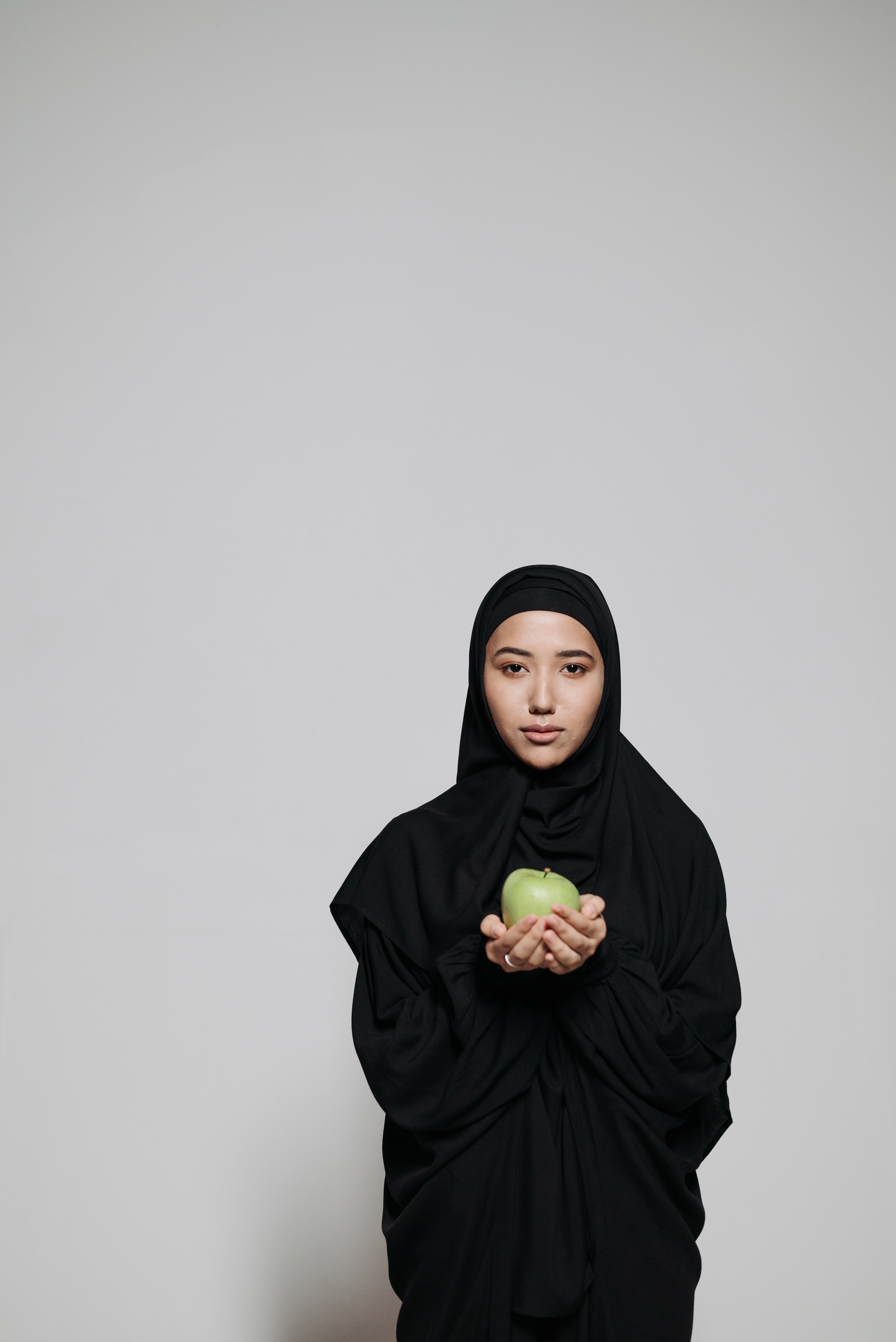 Woman in Black Abaya and Hijab Holding Green Apple Fruit · Free Stock Photo