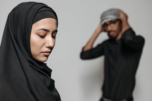 Free Close-up portrait of a woman wearing a hijab with a man in the background, creating a moody studio scene. Stock Photo