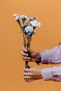 Close-up of hands holding a flower bouquet against a peach background, showcasing elegance and simplicity.