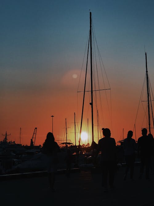 Silhouette of People and Sailboats in the Harbor During Sunset