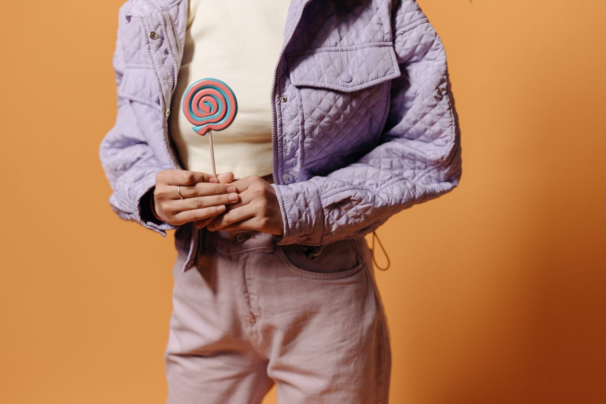 Stylish composition of hands holding a colorful lollipop against an orange background in a studio setup.