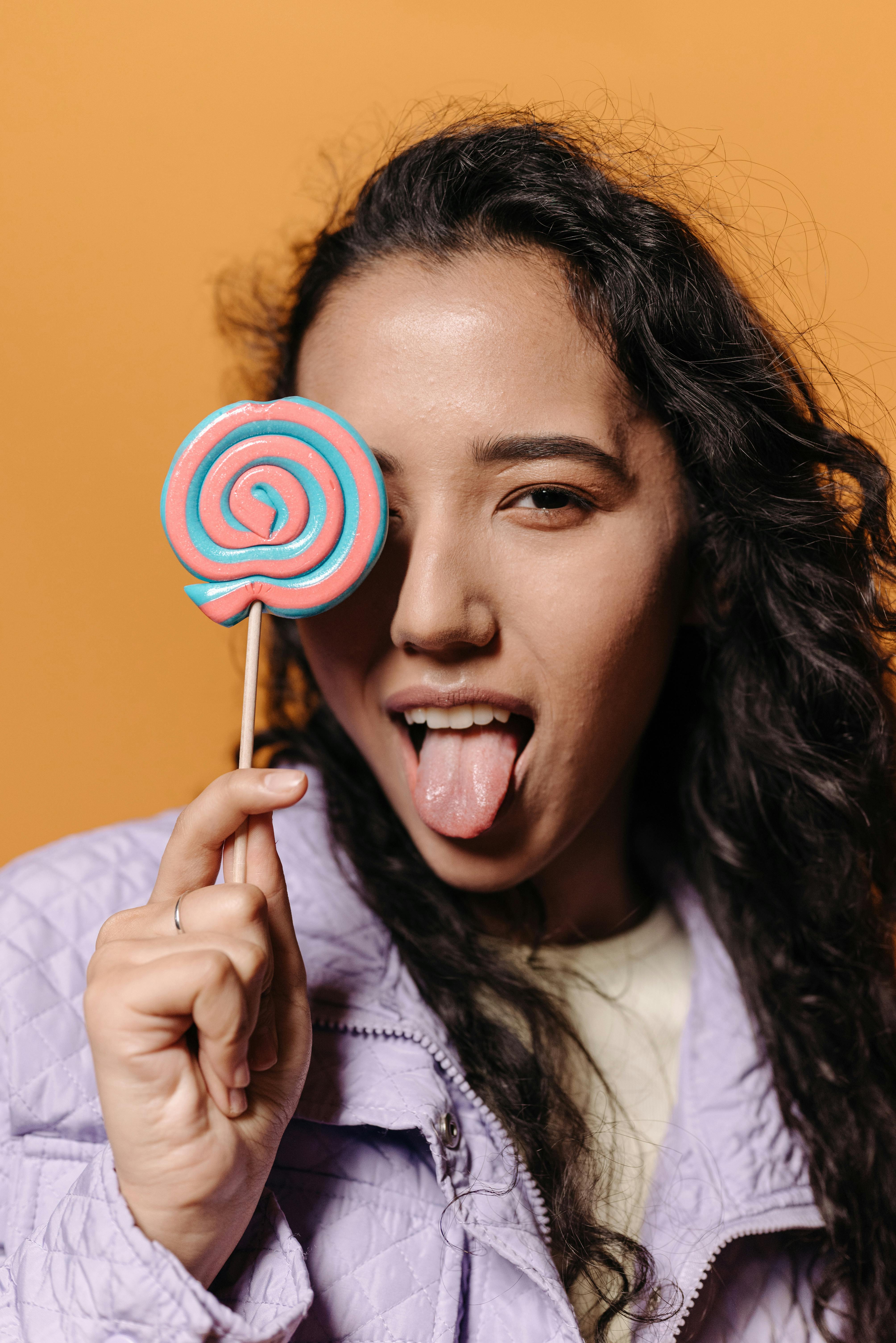 A Woman Holding a Lollipop while Sticking Her Tongue Out · Free Stock Photo