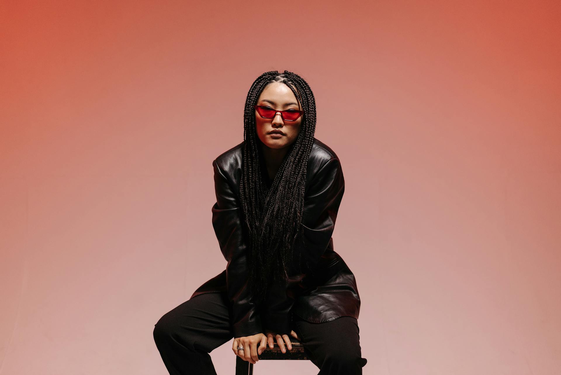 Fashionable woman in black leather with braids and red shades posing in studio.