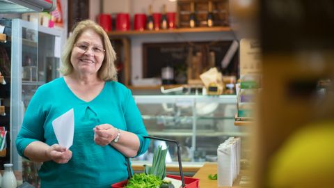 A smiling woman holding a basket in a Portuguese grocery store, enjoying her shopping experience.