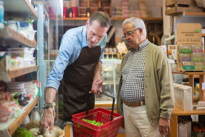 A salesman helps an elderly man with shopping in a local grocery store.