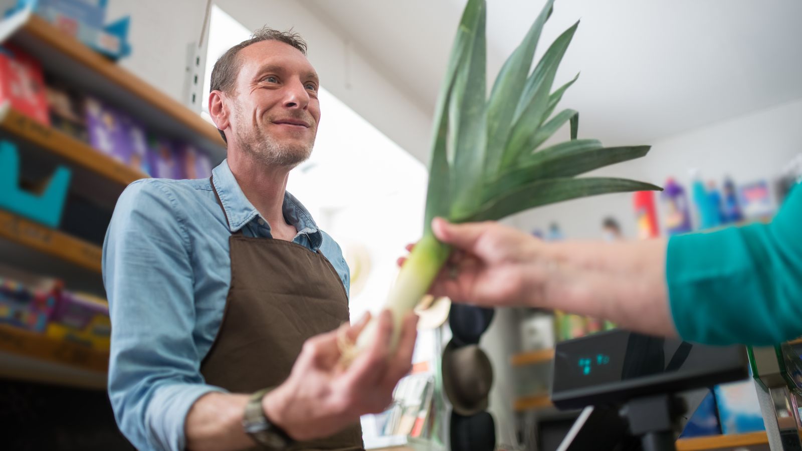 Friendly clerk assisting in vegetable purchase at a grocery store, showcasing personal customer service.