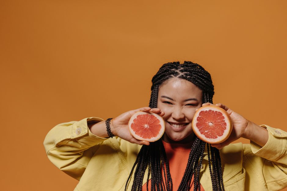 Bright and cheerful portrait of a woman holding grapefruit slices against an orange backdrop, showcasing energy and freshness.