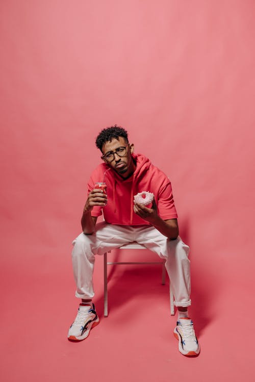 Man Sitting on Chair While Holding a Drink and a Donut