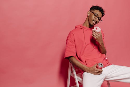 Man in Red Hoodie and White Pants Eating Donut