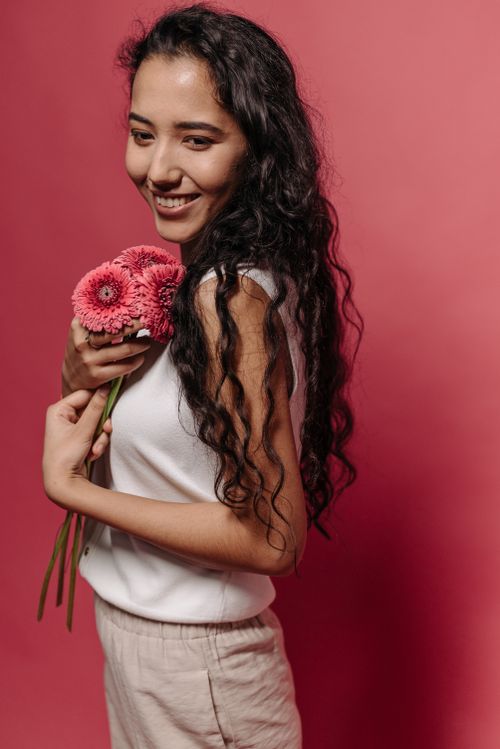 Free Portrait of a smiling woman holding pink gerbera flowers against a red background. Stock Photo
