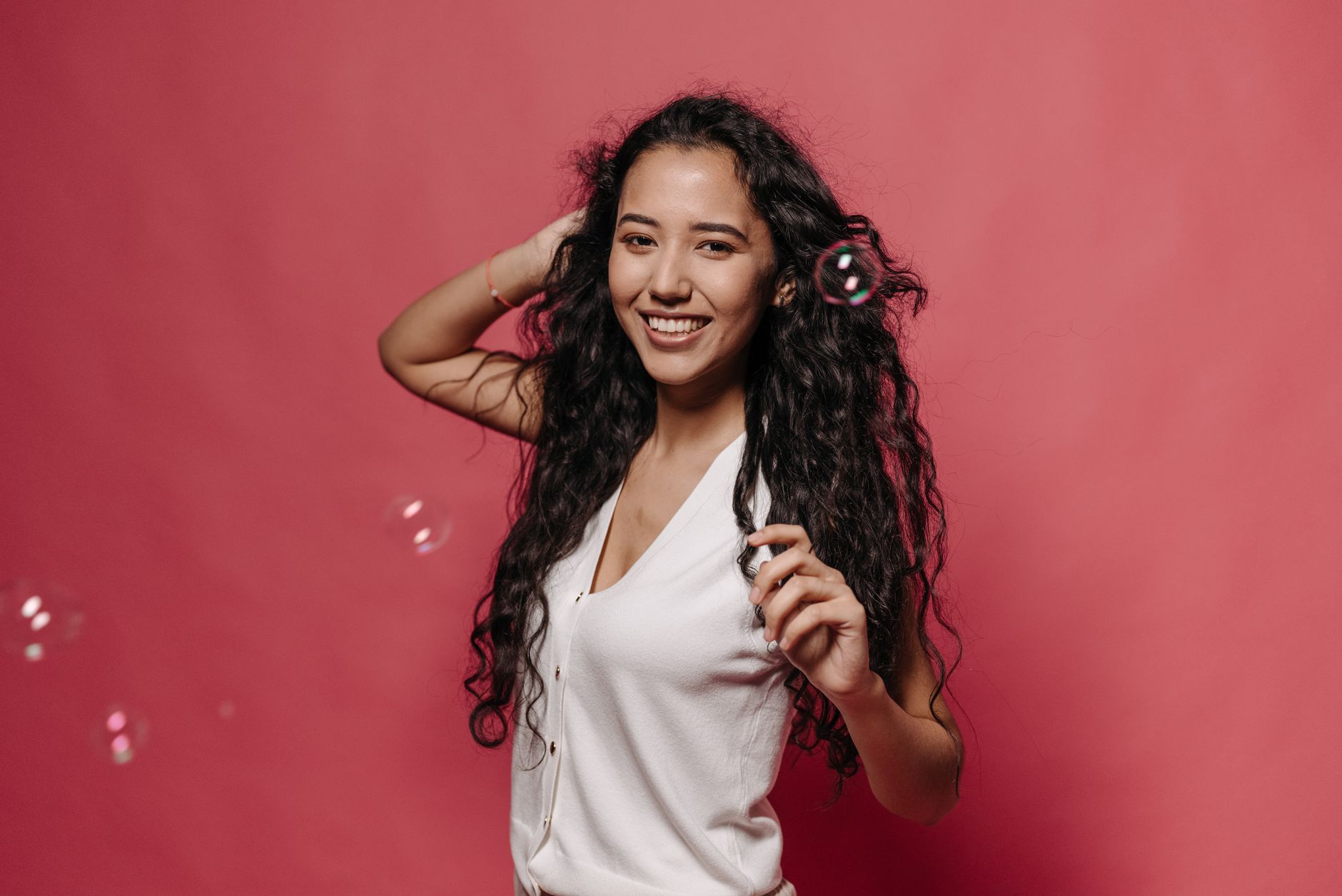 Portrait of a young woman smiling with bubbles against a pink backdrop.