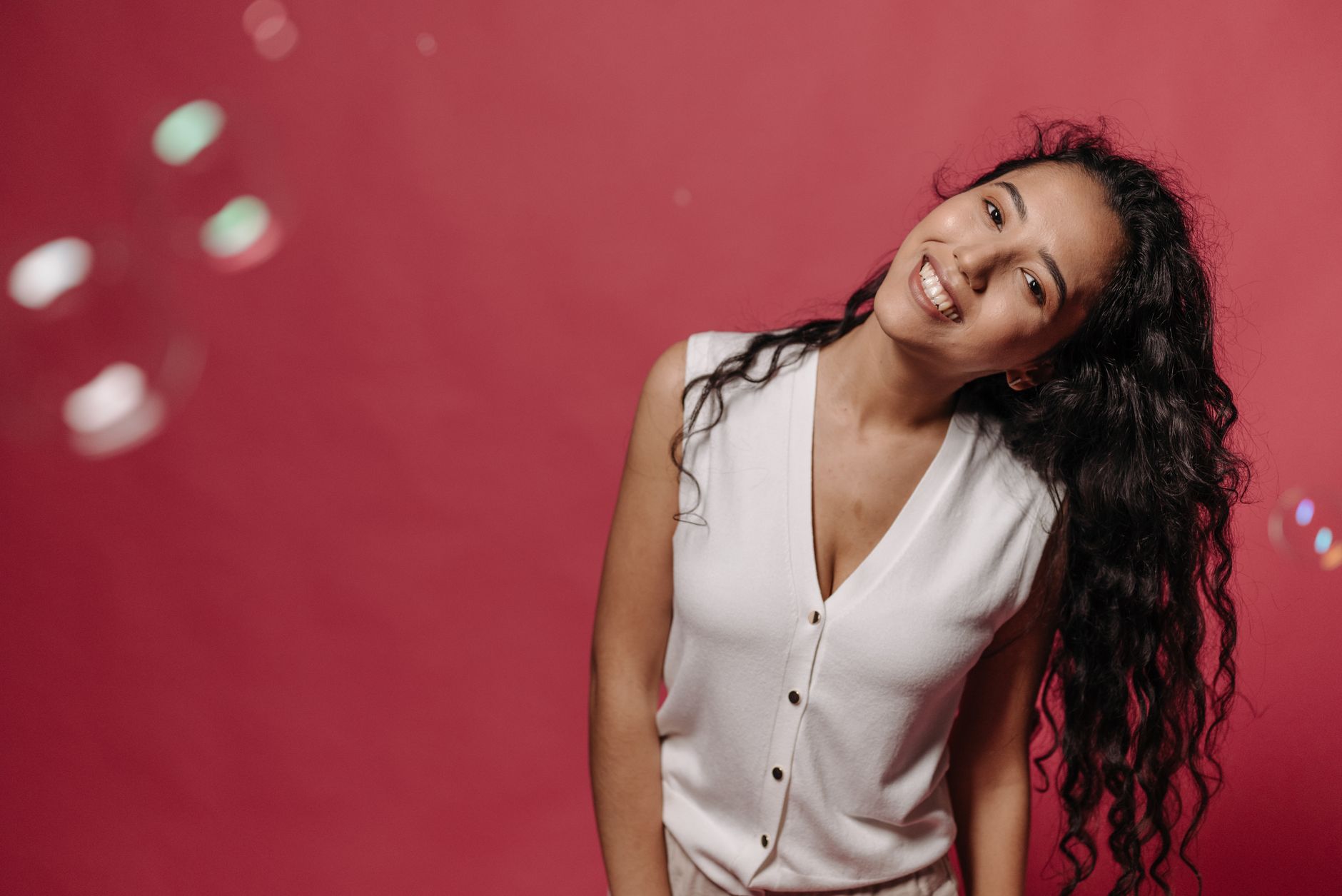 Smiling woman in a sleeveless top posing in a studio with a vibrant red background.