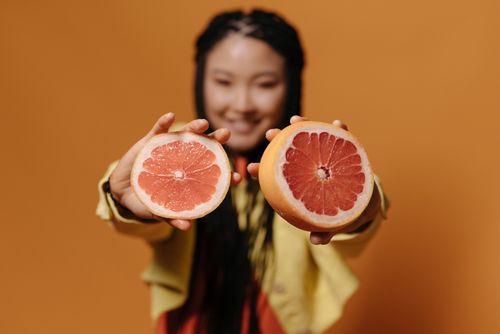 Free Bright studio shot featuring a woman holding sliced grapefruit with an orange background. Stock Photo