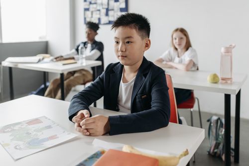 Free Young student focused in class, sitting at a desk with peers, ready to learn. Stock Photo
