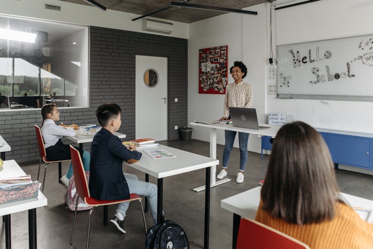 Smiling Teacher Discussing And Standing In Front Of Students Inside A Classroom