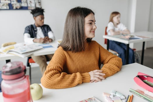 A cheerful student sitting at a desk in a classroom setting, surrounded by peers.