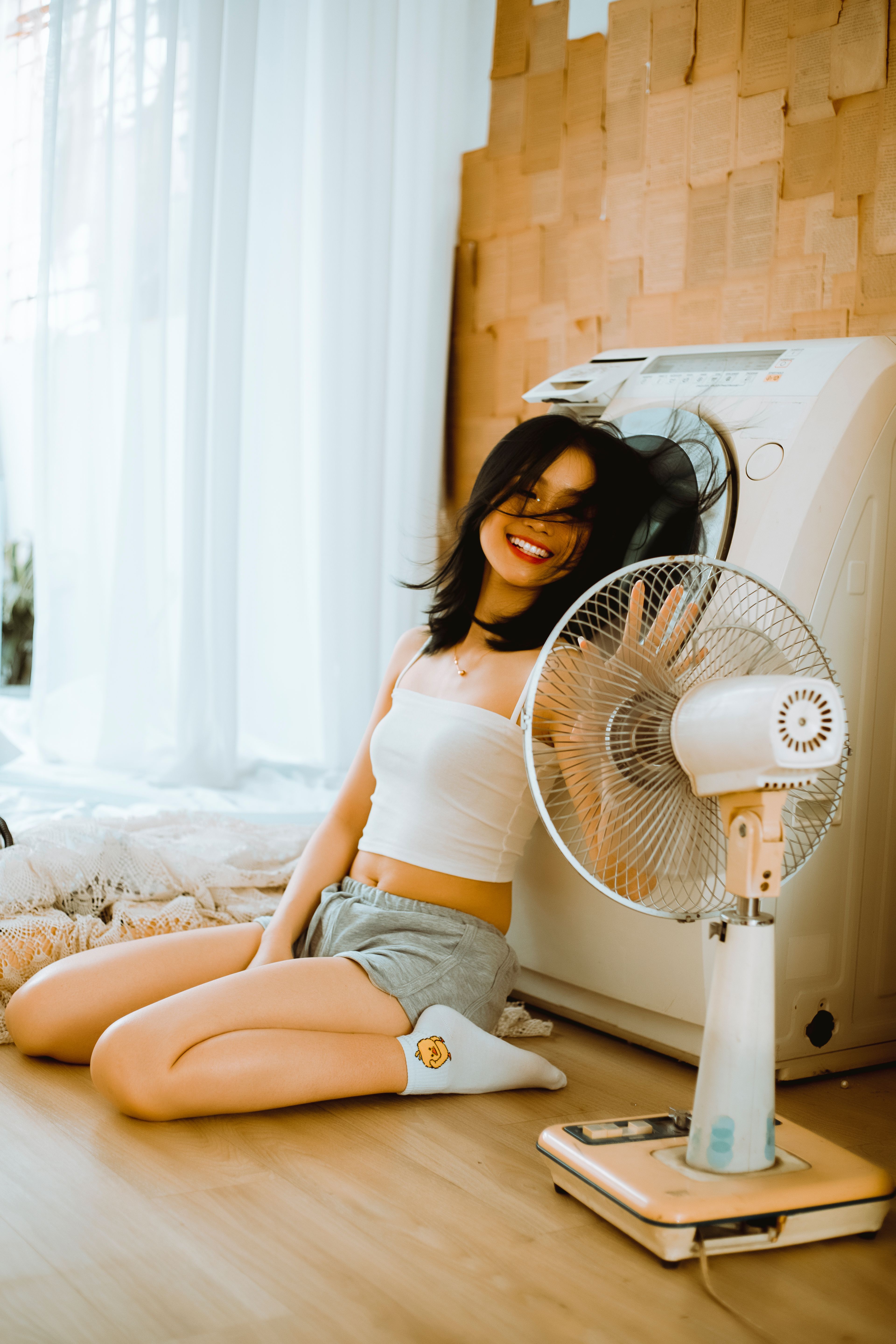 Happy woman sitting indoors smiling and enjoying the breeze from a fan on a warm day.