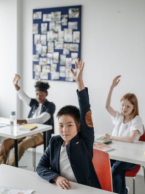 Children raising hands in a modern bright classroom