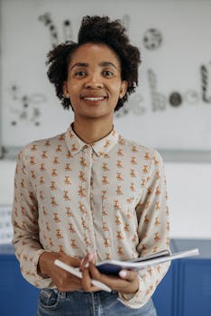 A smiling teacher stands in a classroom holding notes, embodying education and professionalism.