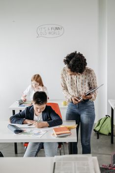 Teacher guiding students in a diverse, modern classroom setting.
