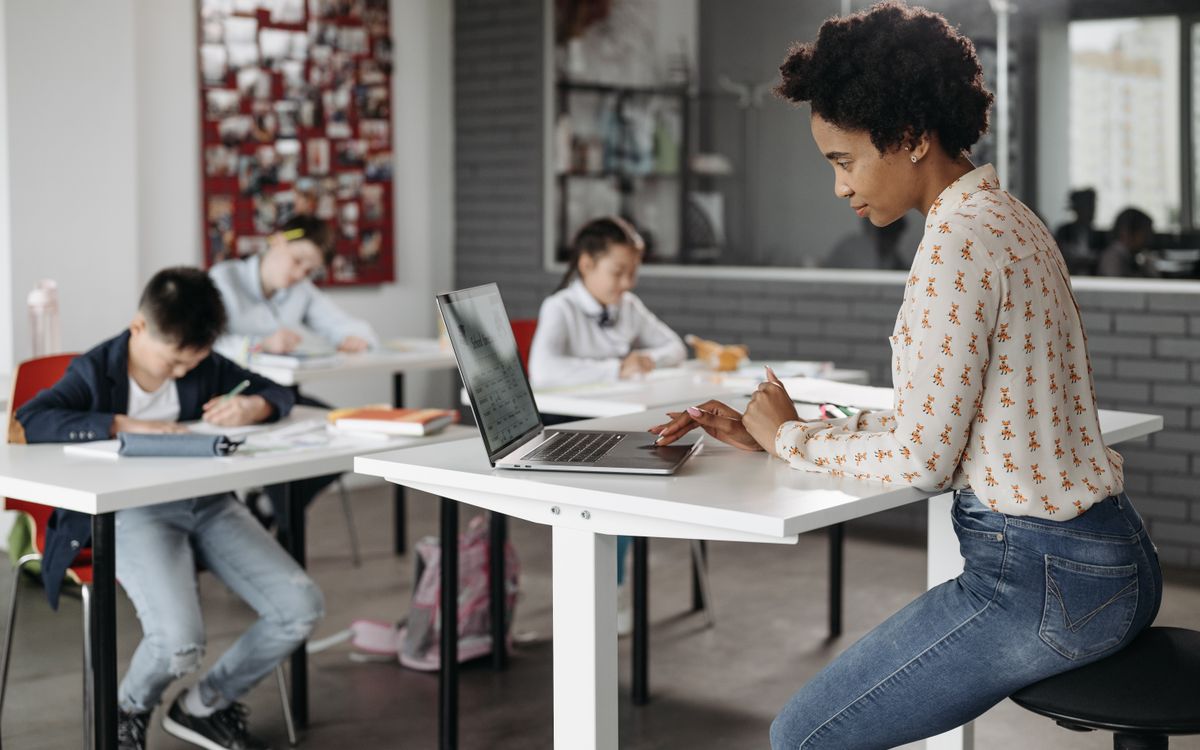 Focused teacher with students working at desks in an indoor classroom environment.