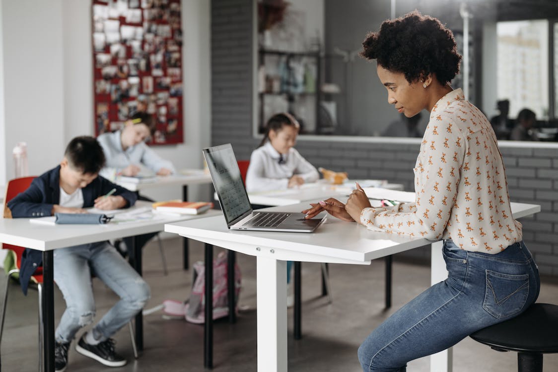 Free A Teacher on Her Laptop While Her Students are Busy Stock Photo