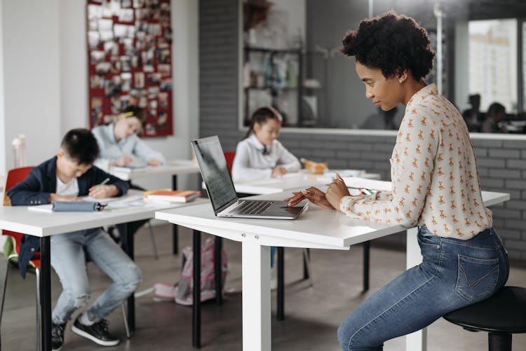 A Teacher On Her Laptop While Her Students Are Busy