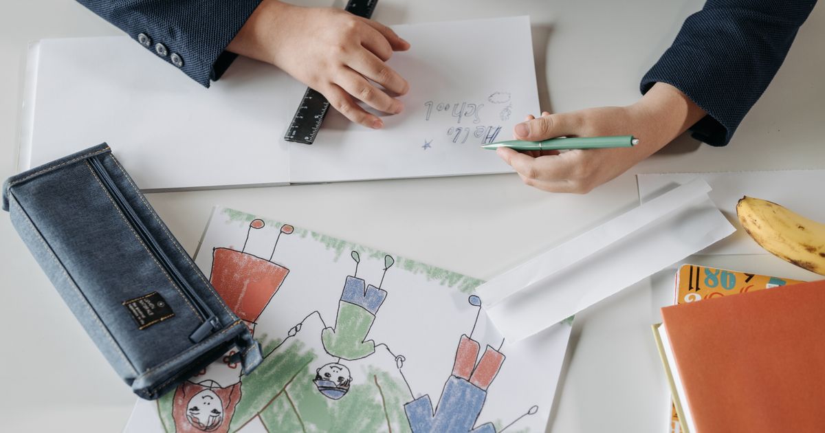 テーブルでノートに書き込む手元と、色鉛筆で描いた絵