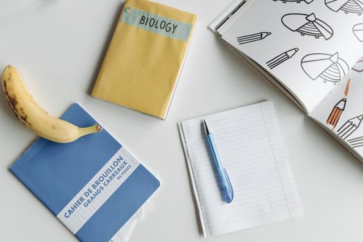 Flat lay of school supplies including notebooks, a banana, and a pen on a white table for study inspiration.