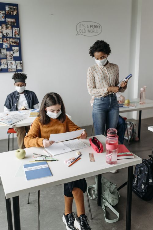 Free Children and teacher in a classroom practicing safety with face masks during a lesson. Stock Photo