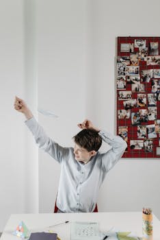 Young school boy in classroom throwing a paper airplane, engaging in playful activity.